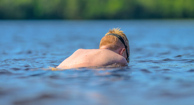Swimmer resting face down in dark lake water with quiet summer mood.