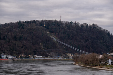 Fototapeta premium Construction of the modern A26 suspension bridge cables over the Danube River in Linz, Austria, featuring the forested hill landscape during autumn.