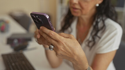 Fototapeta premium Woman holding purple smartphone, fingers tapping touchscreen at desk in building; daily routine concentration.