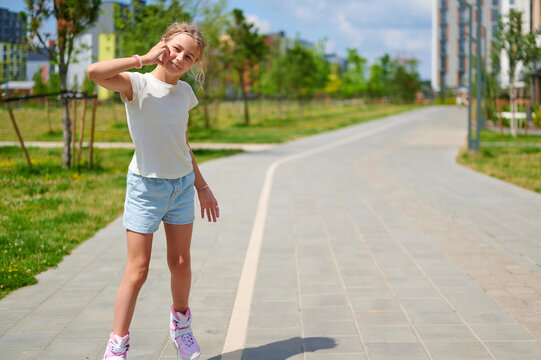 Happy young girl talking on a smartphone while roller skating in a sunny city park