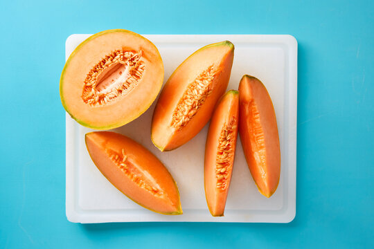 Fresh cantaloupe melon slices on a white cutting board over blue background. Healthy summer fruit.