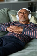 Fototapeta premium Older man lying on sofa with headphones for relaxation background and meditation banner design