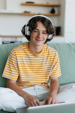 Teen boy in yellow striped shirt wearing headphones on a couch using a laptop for online learning and relaxed lifestyle background or social banner
