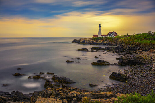 Long exposure seascape of Portland Head Lighthouse on the rocky Cape Elizabeth coast, glowing at sunset over Casco Bay, Maine, USA.