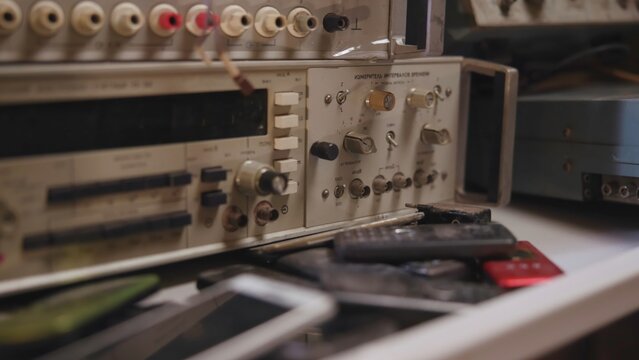 Vintage rack-mounted electronics test panel seen from low angle with rotary knobs, toggle switches, connectors, stacked pushbuttons, and worn metal plastic surfaces in laboratory workshop