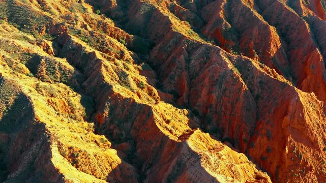 Aerial view of vibrant red clay canyon formations under warm sunlight in Xinjiang.