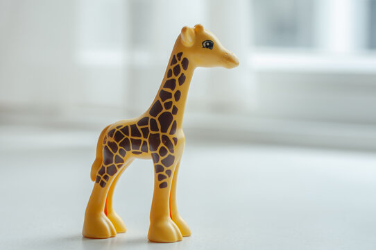 Small giraffe toy standing alone against a bright blurred window background. Minimal composition highlighting wildlife inspired design and children's educational toys.