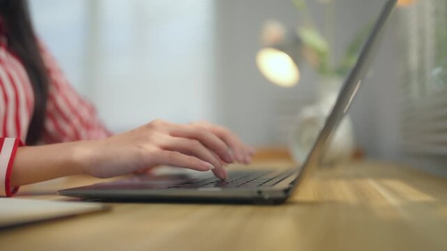 Close up of female hands typing on a laptop keyboard while working on a project in a home office with sunlight