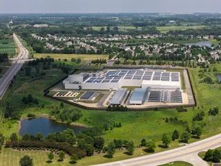 Aerial view of a data center with solar panels on the roof, AI center structure surrounded by roads and green countryside areas  © marchello74