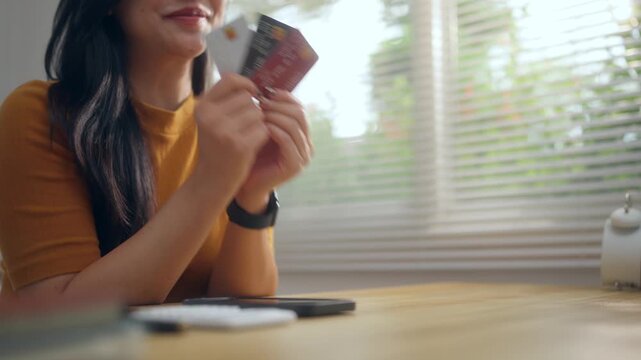 Smiling woman choosing a credit card for online payment and shopping while sitting at her home desk