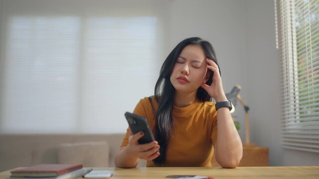 Stressed asian woman checking credit card debt and payments on her smartphone becoming upset and worried about her finances