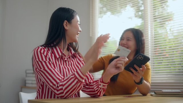 Happy asian friends shopping online with smartphone and credit card giving a high five after a successful payment transaction