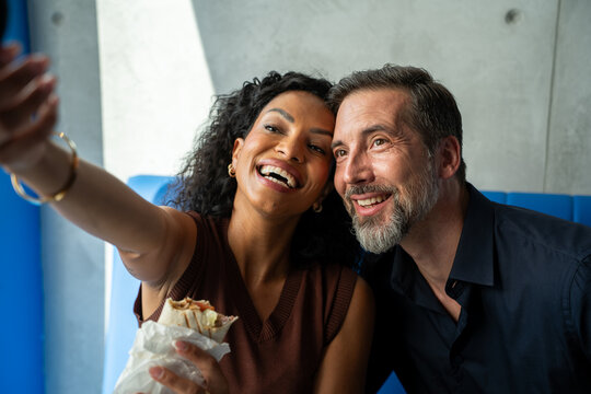 Portrait of a diverse romantic couple in restaurant having lunch and using a mobile phone and taking a selfie