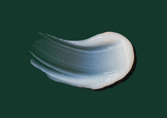Obraz premium A smooth stroke of white cosmetic cream texture isolated on dark green background, soft gel or lotion swatch closeup