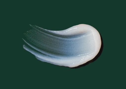 A smooth stroke of white cosmetic cream texture isolated on dark green background, soft gel or lotion swatch closeup