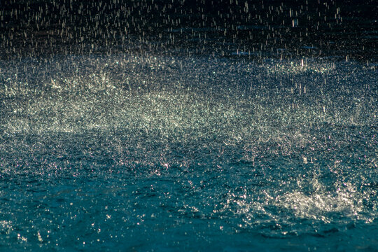 Close-up of intense rain drops falling and creating splashes on a deep blue water surface during a tropical storm in Brazil. Perfect for concepts of nature, weather, 