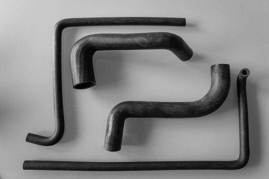 Black and white flat-lay of assorted molded rubber automotive hoses in varying shapes and sizes, arranged on a plain gray background, showing coolant and radiator hose parts for a vehicle