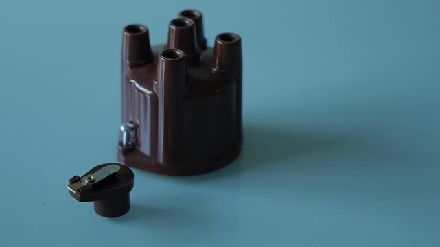 A brown plastic distributor cap with five spark plug terminals paired with its matching rotor arm, photographed on a plain gray background as automotive ignition system parts