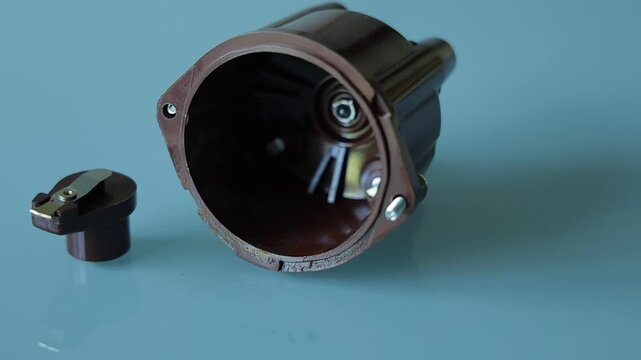 A brown plastic distributor cap with five spark plug terminals paired with its matching rotor arm, photographed on a plain gray background as automotive ignition system parts
