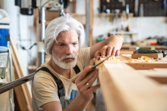 Experienced man crafter working with vintage wooden door at workbench mindfully checking surface, thoughtful craftsman woodworker in carpentry workshop examining wood during reconstruction process.