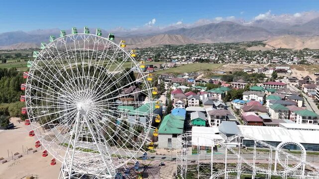 Ferris wheel by Issyk-Kul Lake with scenic mountains in the background, a popular tourist spot.