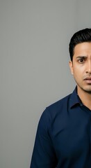 Obraz premium Young Middle Eastern man wearing navy blue shirt against neutral gray background, professional headshot for corporate and business applications.
