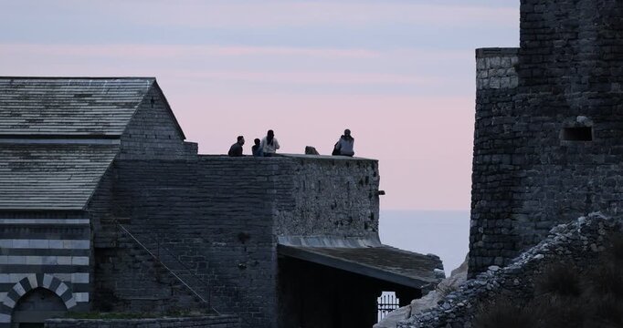 Vista di persone sedute sugli storici muri in pietra della terrazza della Chiesa di San Pietro a Porto Venere, in Liguria, Italia.