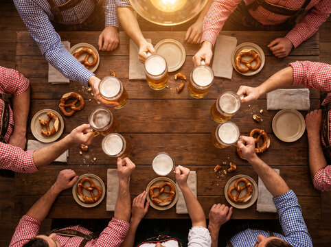 Top down shot of hands raising beer mugs in toast over table with pretzels