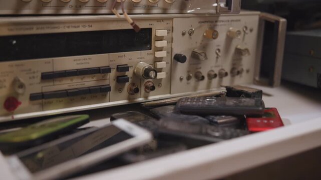 Vintage rack-mounted electronics test panel seen from low angle with rotary knobs, toggle switches, connectors, stacked pushbuttons, and worn metal plastic surfaces in laboratory workshop