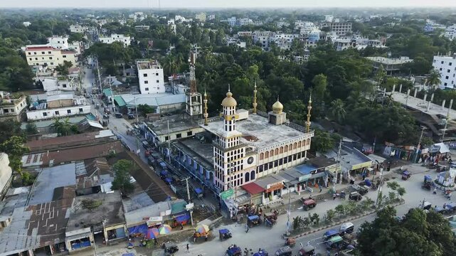 Aerial view of a city neighborhood with a large mosque, busy street traffic, market stalls and dense trees, showing everyday urban life in a tropical setting.