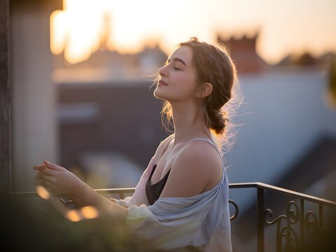 Retrato de mujer joven contemplativa disfrutando de la puesta de sol en un balc&oacute;n urbano