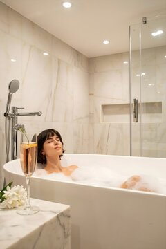 Mujer joven relaj&aacute;ndose con los ojos cerrados en un ba&ntilde;o de burbujas en una tina moderna de lujo