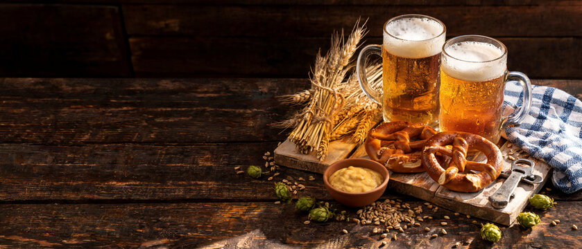 Oktoberfest beer and pretzels on rustic board with wheat and hops, banner copy space background