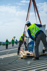 Naklejka premium A photovoltaic technician wearing a safety vest and hard hat skilfully counts the delivered photovoltaic panels on the sweeping metal roof of a manufacturing plant in Southeast Asia.