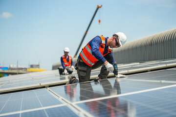 Fototapeta premium A renewable energy specialist in reflective workwear and helmet confidently secures module clamps methodically along the row on a large corrugated factory rooftop under the tropical sun.