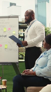 Vertical video: Diverse business people explaining vision implementation with sticky notes, gesturing with open hands during outdoor presentation, informal discussion.