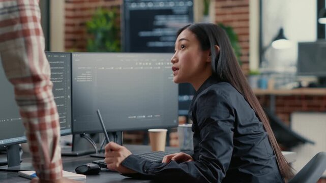 Database developer reviews programming information at a computer workstation, connecting source code, systems and development productivity, during active software engineering.