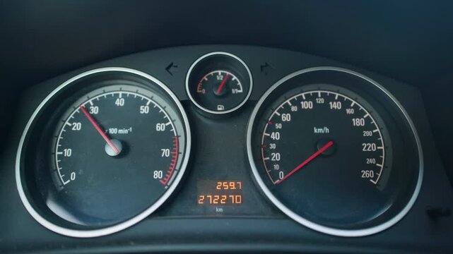 Car instrument cluster with circular speedometer, tachometer, fuel gauge, and digital odometer, illuminated inside dark vehicle interior with clean markings, metallic trim, and subtle needle movement