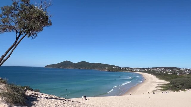 A breathtaking aerial view of the iconic One Mile Sand Dune towering over the pristine coastline of Forster, New South Wales. This massive natural sand hill meets the turqu