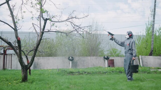 Worker in protective coverall trimming backyard tree with gas trimmer beside grassy lawn, fence, and cloudy sky, showing careful seasonal garden maintenance in suburban setting