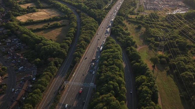 Aerial drone footage pulling back above the M6 motorway near Birmingham, England, revealing heavy traffic congestion caused by a road accident. One carriageway flows normally while the opposite direct
