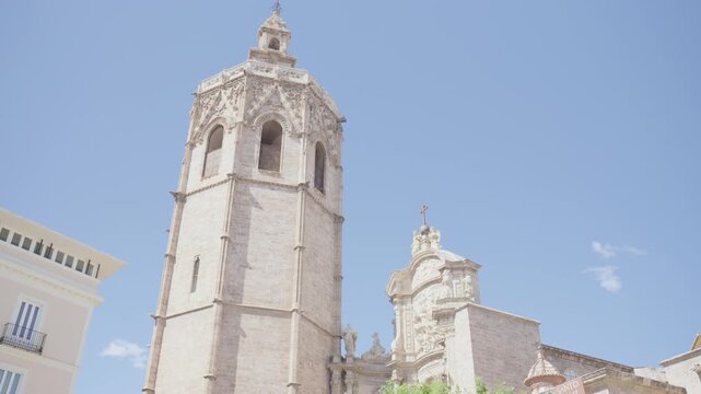 Low angle view of historic stone church bell tower and ornate dome against clear pastel blue sky, with carved Gothic details, arched openings, pinnacles, and elegant heritage architecture