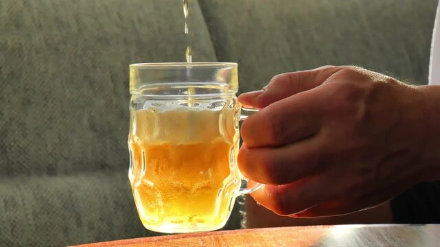 Foamy beer in a glass mug. Beer is being poured into a mug.Man Holding Glass Mug of Cold Beer While Relaxing at Home. 4k footage