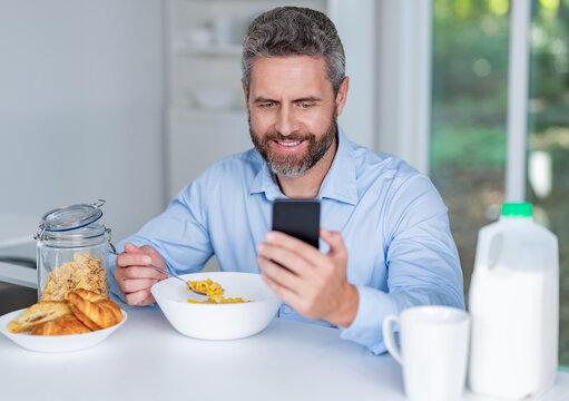 Breakfast in kitchen. Man eating cereal checking message. Healthy food online. Morning news. Man eat morning breakfast in kitchen. Business man eating morning breakfast. Morning at home with phone