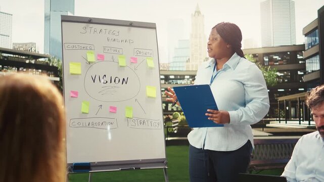 Black businesswoman with clipboard pointing to vision board with sticky notes, leading presentation and discussion in strategy meeting at outdoor workshop, informal meeting, for business planning.