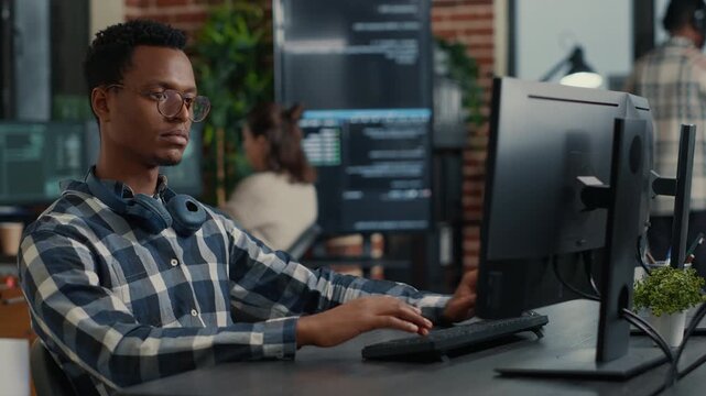 Cybersecurity programmer types programming code on an office keyboard, turning from the monitor during software development work, during a professional debugging session.