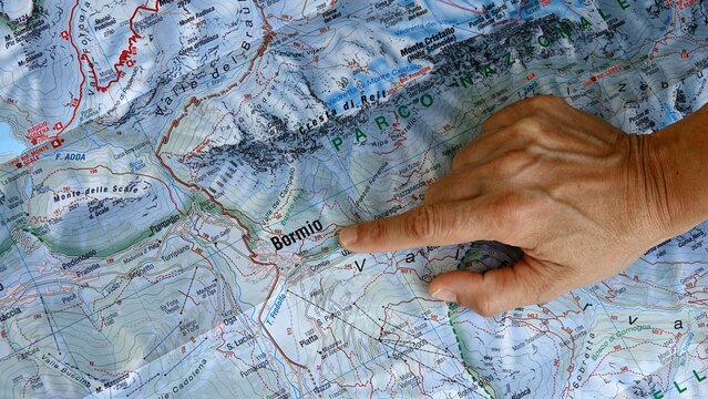Hand pointing to a topographic map of Stelvio National Park in the Italian Alps. A person's hand indicates a specific location on a detailed topographical map of the mountainous Stelvio National Park 