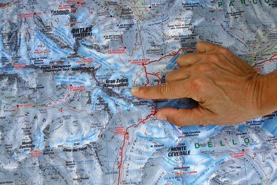 Hand pointing to a topographic map of Stelvio National Park in the Italian Alps. A person's hand indicates a specific location on a detailed topographical map of the mountainous Stelvio National Park 