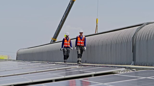 Two construction professionals working together to install solar panels on a rooftop using a crane for support