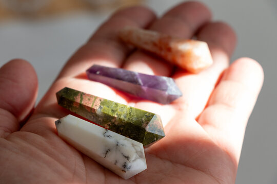 puntas de cristales y gemas naturales, &oacute;palo dendrita, unakita, amatista, piedra del sol sostenidos en la palma de la mano iluminadas por suaves rayos del sol